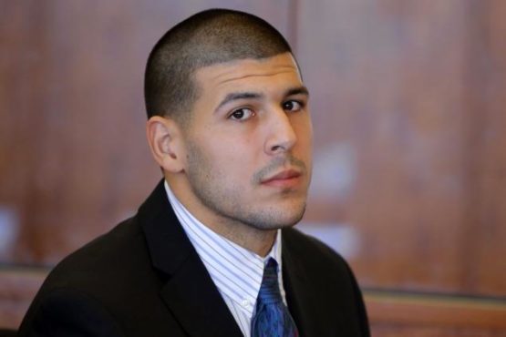 Aaron Hernandez wearing a black suit jacket, striped collared shirt, and blue tie.