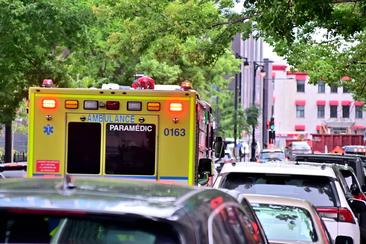 Ambulance caught in urban traffic amidst green trees, focused on emergency response.